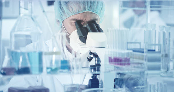 istock Man in a specialist mask and hat looks into a microscope 1211333964
