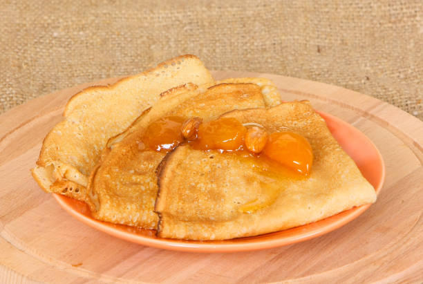 istock Fried pancakes folded in a triangle with apricot jam lie on an orange plate. 1211335064