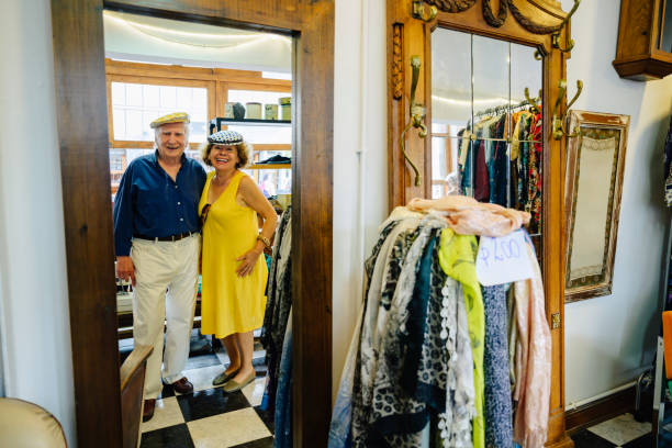 Smiling senior couple in 70s and 80s trying on flat caps in secondhand store while enjoying day of shopping in Buenos Aires.
