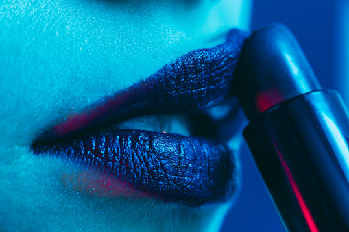 Close up of woman applying lipstick. Neon lights.