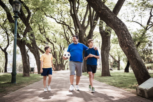 father and sons playing soccer in the park - healthy lifestyle nature sports shoe childhood imagens e fotografias de stock