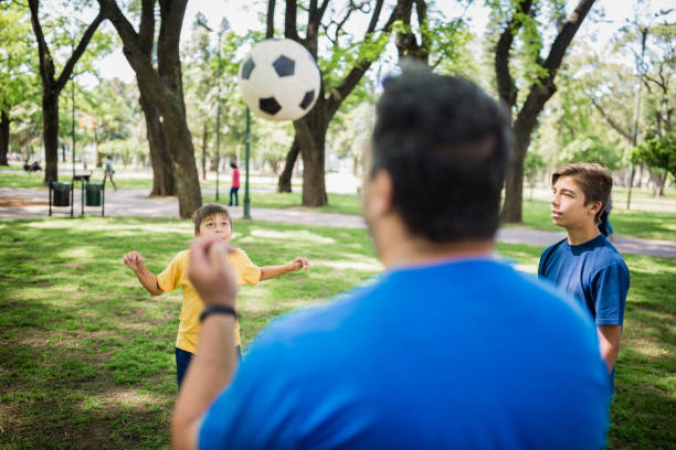 istock Father and sons playing soccer in the park 1211338323