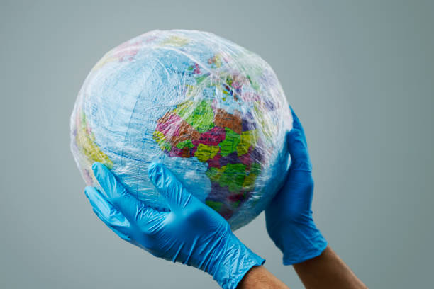 doctor with a world globe wrapped in plastic a doctor man wearing blue surgical gloves holding a world globe wrapped in plastic, depicting the plastic contamination or the protection against the epidemic infectious diseases or the air pollution 2273 stock pictures, royalty-free photos & images