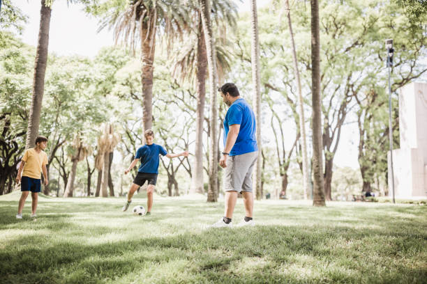 istock Father and sons playing soccer in the park 1211338429