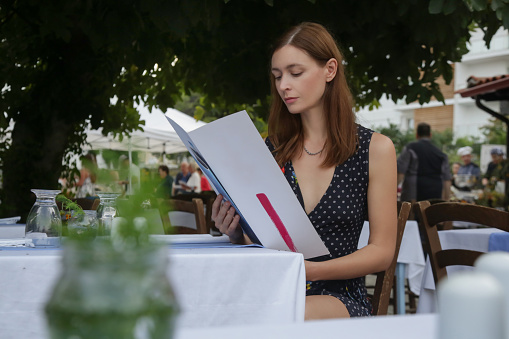 Young woman reading food menu at the outdoor restaurant