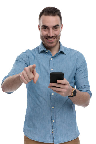 istock Happy casual man holding phone, smiling and pointing 1211344494