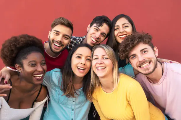 Photo of Group multiracial people having fun outdoor - Happy mixed race friends sharing time together - Youth millennial generation and multiethnic teenagers lifestyle concept - Red Background