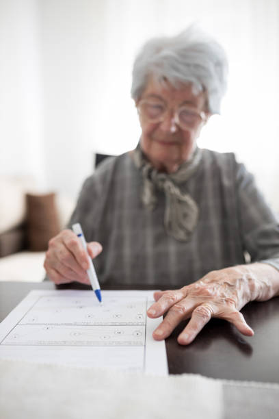 Close-up of a serious senior woman's hands doing Alzheimer's disease or dementia self assessment test at home Close-up of a serious gray haired senior Caucasian woman's hands doing Alzheimer's disease or dementia self assessment test at home by connecting numbers and letters. Focus on foreground atrophy photos stock pictures, royalty-free photos & images