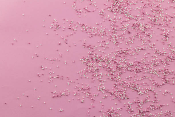 istock Sprinkle background with pink and white cake topping sprinkles scattered on pale pink backdrop with space for text 1211350000