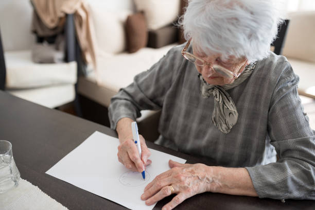 High angle view of a senior woman doing Alzheimer's disease cognitive functions self assessment test at home High angle view of a senior Caucasian woman doing Alzheimer's disease cognitive functions clock drawing self assessment test at home with positive results suggesting illness atrophy photos stock pictures, royalty-free photos & images