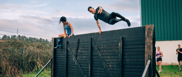 participantes em pista de obstáculos escalando parede - obstacle course - fotografias e filmes do acervo