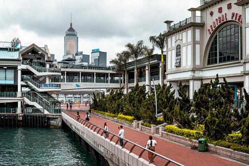 Promenade at Hong Kong Central Pier, people walking, Maritime Museum and skyline in the background.