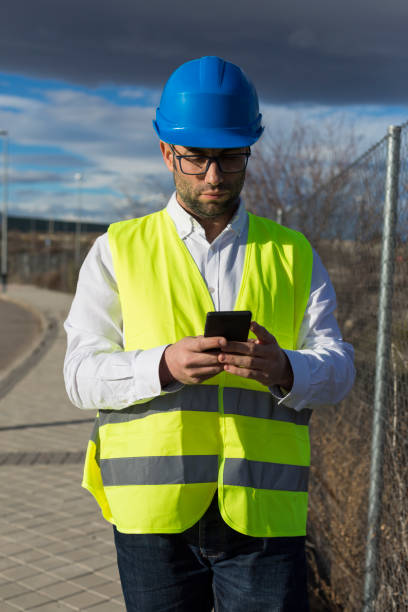 architekt lub inżynier człowiek ręce za pomocą telefonu komórkowego na placu budowy. koncepcja pracy. noszenie odzieży ochronnej - people in a row in a row business office worker zdjęcia i obrazy z banku zdjęć