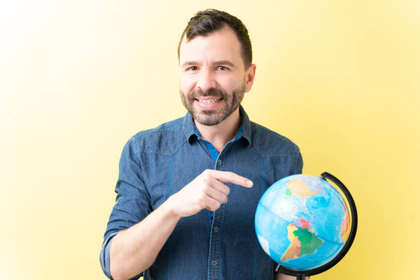 istock Latin Adult Man Is Pointing At World Map 1211355842