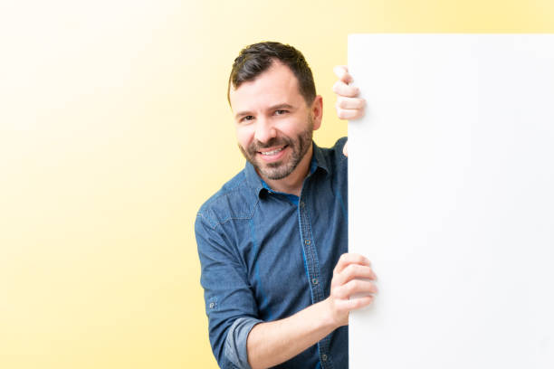 istock Smiling Latin Man Is Behind White Billboard 1211355884