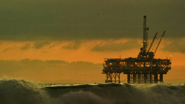 wellen quellen in der nähe von huntington beach in südkalifornien mit einer offshore-ölbohrplattform am horizont bei sonnenuntergang unter einem dramatischen, stürmischen himmel - oil rig sea oil storm stock-fotos und bilder