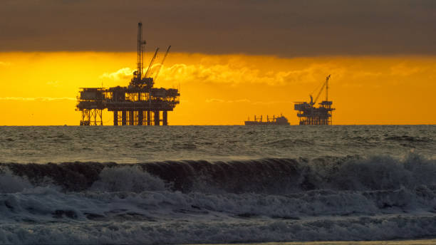 파도가 해안으로 추락하는 여러 실루엣의 해양 석유 시추 장비 플랫폼과 드라마틱한 폭풍우 하늘 아래 일몰 의 거리에서 수평선에 석유 (석유) 유조선 - oil rig sea oil storm 뉴스 사진 이미지