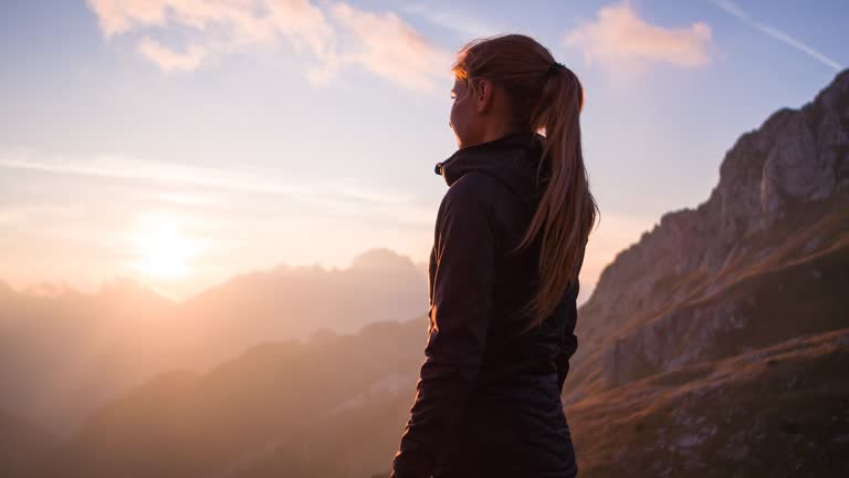 Woman standing on top of mountain, enjoying breathtaking view at sunset