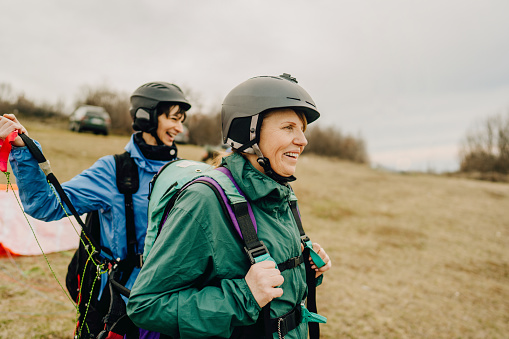 Photo of smiling senior woman and her instructor before the flight with a paraglider