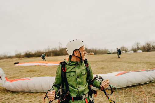 Photo of a smiling senior man ready for take off with his paraglider