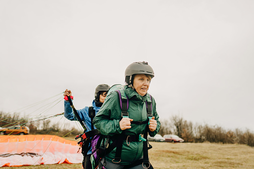 Photo of smiling senior woman and her instructor before the flight with a paraglider