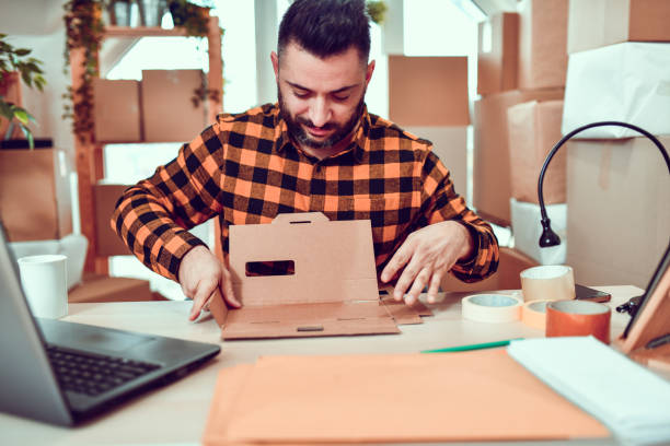istock Handsome Male Folding Cardboard Package In Delivery Office 1211371672