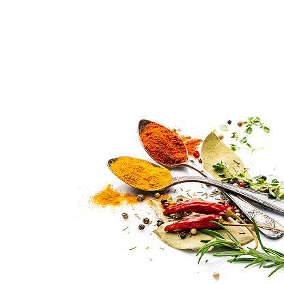 Top view of two old spoons with spices and herbs shot on white background. Spices and herb included are turmeric, bay leaf curry powder, peppercorns, paprika, rosemary and others. The composition is at the right of an horizontal frame leaving useful copy space for text and/or logo at the left. High resolution 42Mp studio digital capture taken with Sony A7rII and Sony FE 90mm f2.8 macro G OSS lens