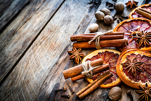 Scented spices: dried orange slices, clove, cinnamon, star anise and nutmeg shot on rustic wooden table. The composition is at the right of an horizontal frame leaving useful copy space for text and/or logo at the left. Selective focus on foreground. Predominant colors are orange and brown. High resolution 42Mp studio digital capture taken with SONY A7rII and Zeiss Batis 40mm F2.0 CF lens