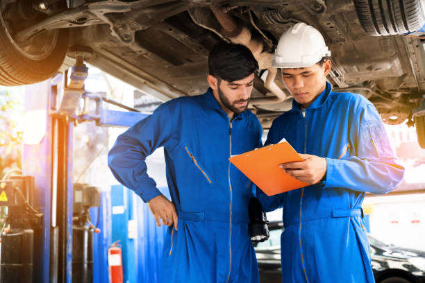 istock Mechanic in blue work wear uniform inspects the car bottom with his assistant. Automobile repairing service, Professional occupation teamwork. Vehicle maintenance. 1211375459
