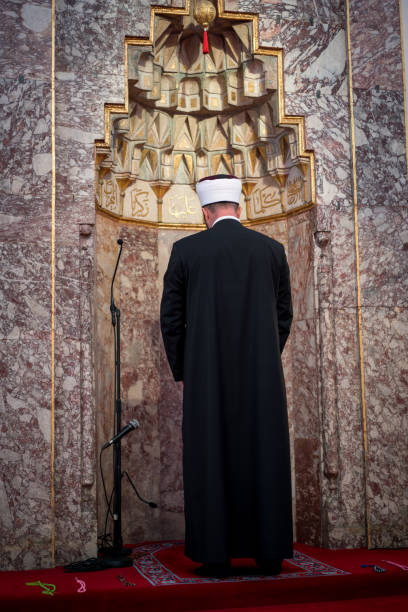 Emam in mosque with verses from Kuran on the wall Emam in mosque with verses from Kuran on the wall azan stock pictures, royalty-free photos & images