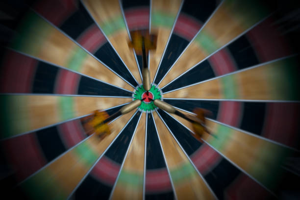 Close-up of an electronic dartboard illuminated in dim lighting. The dartboard's bullseye and surrounding scoring areas are visible, showcasing intricate patterns and numbers. Soft shadows create a moody atmosphere, highlighting the details of the game device.