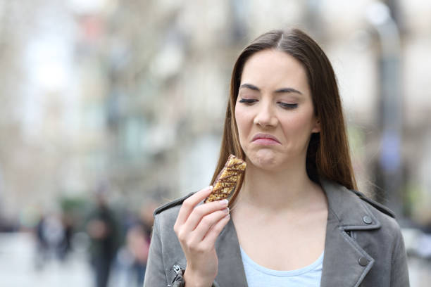 Disgusted woman looking at snack bar on city street Front view portrait of a disgusted woman looking at snack cereal bar on a city street disgust stock pictures, royalty-free photos & images
