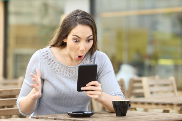 Amazed girl looking at her phone on a cafe terrace Amazed girl looking surprised at her smart phone on a cafe terrace i see you meme stock pictures, royalty-free photos & images