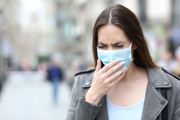 istock Sick woman with protective mask coughing on street 1211385184