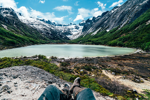 Pov view of a man's legs and shoes near Laguna Esmeralda, Emerald lake - Ushuaia, Patagonia - Argentina. Tierra del Fuego province.