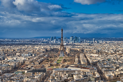Paris, France - February 25, 2020 - Aerial view of the Eiffel Tower under a cloudy sky. In the foreground, the roofs of Paris, including the military school, the Champ de Mars and the Eiffel Tower are visible. In the background, the rest of Paris including the La Défense business district are visible.