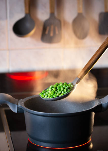 Green boiled peas on kitchen spoon with steam
