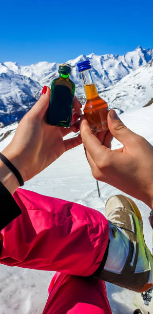 ハイリゲンブルート - 背景として山とアルコールの小さなボトルを保持しているカップル - snow skiing apres ski couple ストックフォトと画像