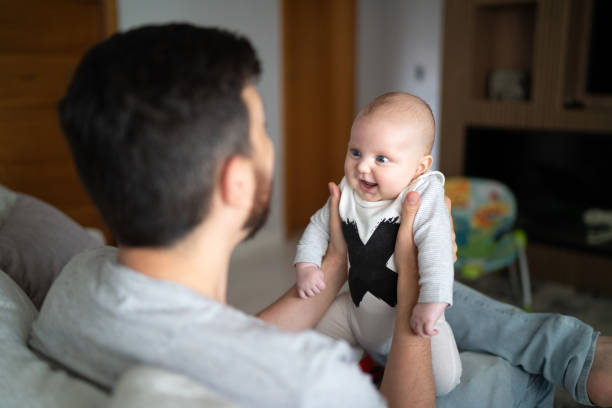 istock Cheerful father playing and holds baby on sofa at home 1211406718