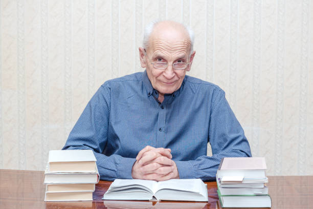 istock old man sits at a table and looks out from under his glasses 1211415808