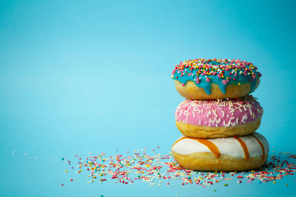 istock Donuts (doughnuts) of different colors on a blue background with multi-colored festive sugar sprinkles. Holiday and sweets, baking for children, sugar concept 1211418067