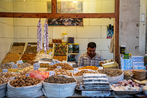 Iraq, Iraqi Kurdistan, Arbil, Erbil. In the bazaar, an old man with a red scarf is buying some delicacies from a shop.