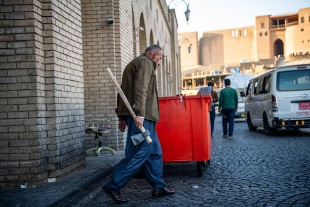 Iraq, Iraqi Kurdistan, Arbil, Erbil. In the background is Erbil Qalat citadel at sunset. A man is crossing the road with an axe