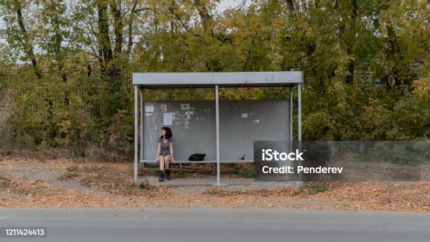 A Lonely Girl In A Dress And Boots Sits At A Bus Stop Stock Photo - Download Image Now