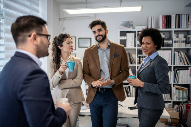 istock Group of smiling colleagues standing at workplace, chatting and drinking coffee on pause 1211424732