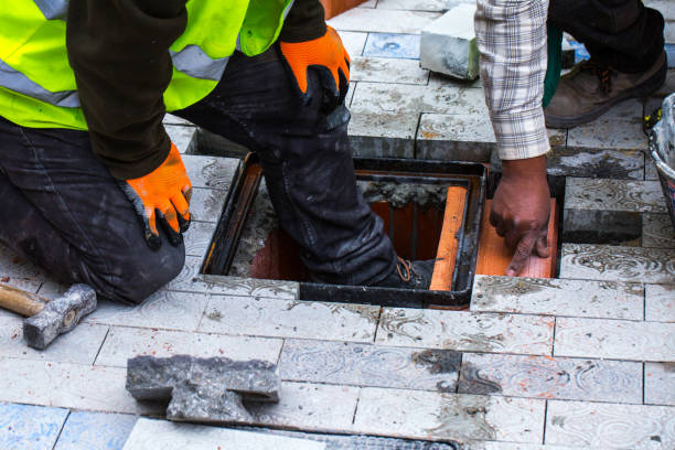 istock Construction work on pavement. Installation of concrete paver blocks on the sidewalk. Workers do the installation of the well hatch for engineering communications in the pavement. 1211425651