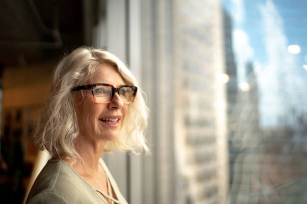 mujer de negocios madura mirando por la ventana - leadership business women senior adult fotografías e imágenes de stock