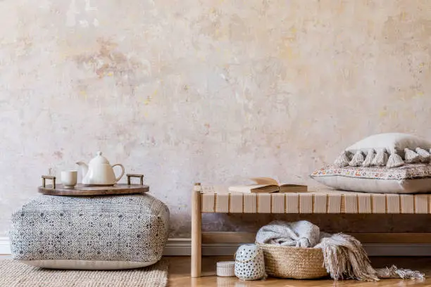 Photo of Stylish oriental living room interior with beige chaise longue, boho decoration, big pouf with wooden tray and tea pot, book and elegant personal accessories. Wabi sabi concept. Copy space. Template