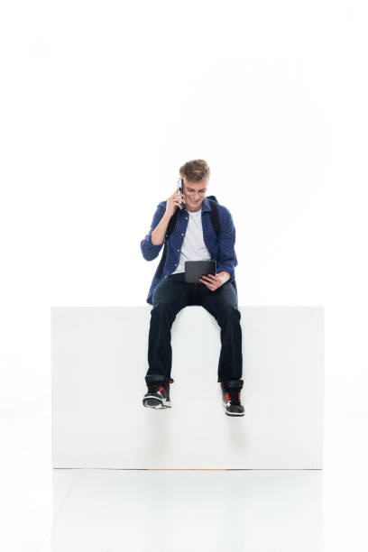istock Caucasian boys resting in front of white background wearing jeans and using touch screen 1211431371