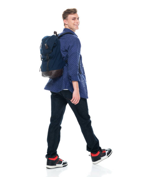 istock Caucasian boys high school student walking in front of white background wearing backpack and holding bag 1211432104